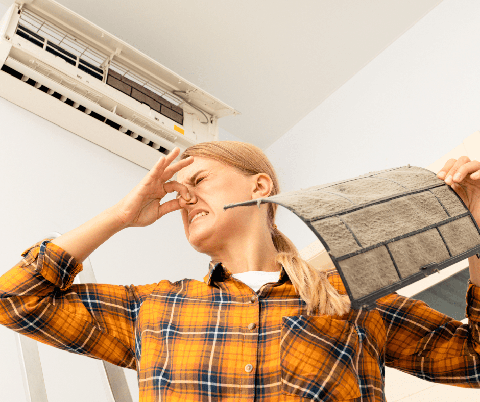 Person holding a dirty air filter which is causing a bad smell in HVAC system.